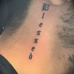 Фото тату надписи 'Blessed' на шее мужчины. Черная типографская татуировка, выполненная аккуратным шрифтом, вертикально вдоль шеи.