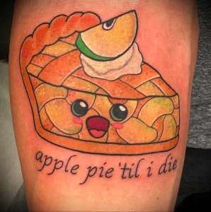 Фото тату куска яблочного пирога с милым личиком и надписью 'apple pie 'til i die'. Яркие цвета и игривый дизайн.