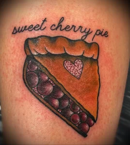 Фото тату с изображением кусочка вишневого пирога и надписью 'sweet cherry pie'. Яркий и сочный рисунок для любителей десертов.
