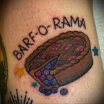Фото тату пирога с черникой и надписью "BARF-O-RAMA" на руке. Яркий и оригинальный рисунок в стиле традиционной татуировки.