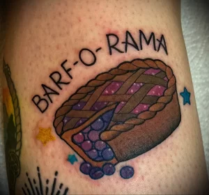 Фото тату пирога с черникой и надписью "BARF-O-RAMA" на руке. Яркий и оригинальный рисунок в стиле традиционной татуировки.