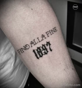 Фото татуировки с надписью "FINO ALLA FINE 1897" на предплечье. Черный цвет, готический шрифт, минималистичный дизайн, сильный и запоминающийся образ.
