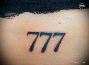 Фото тату с изображением числа "777" на женской коже. Минималистичный дизайн, черные чернила, четкие линии.