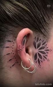 Фото тату: черно-белая татуировка в стиле dotwork, изображающая дерево с птицей на ветке, расположенная вокруг уха. Детализированный и красивый рисунок татуировки.