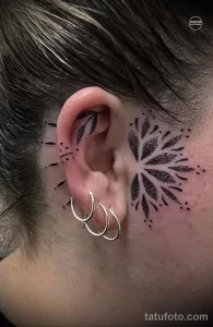 Фото тату: черно-белая татуировка в стиле dotwork, изображающая абстрактное дерево с листьями, расположенная вокруг уха. Оригинальный и сложный рисунок татуировки.