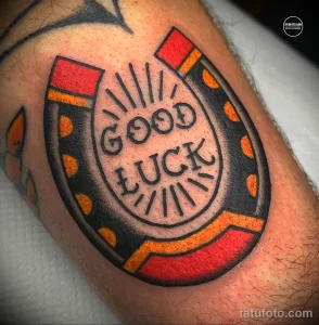 Фото татуировки подковы с надписью 'GOOD LUCK' в стиле олдскул на руке. Яркие цвета, четкие контуры и традиционный дизайн.