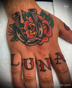 Фото тату на руке: подкова, красная роза и надпись 'LUNA' в стиле олд скул. Яркие цвета и четкие контуры.