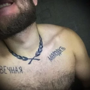 Фото татуировки на мужской груди и шее с изображением лаврового венка и надписи 'Мелодасть'. Рисунок выполнен в графическом стиле с использованием черных линий.
