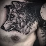 Фото тату волка на груди, выполненного в технике blackwork. Использование только черного цвета и плотной штриховки создает эффектный и стильный рисунок.