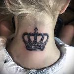 Фото тату: небольшая черная корона на затылке девушки. Простой и элегантный рисунок татуировки, выполненный в минималистичном стиле.