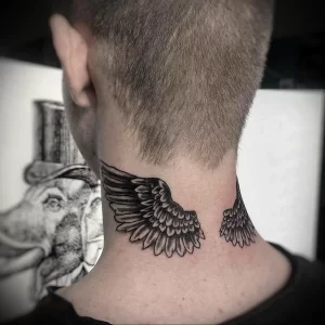 Фото тату двух крыльев на затылке, выполненных в технике blackwork. Рисунок состоит из плотных черных линий и точек, создающих эффект графичного рисунка.