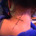 Фото тату креста и надписи 'faith' на шее, выполненного в минималистичном стиле. Небольшой и символичный рисунок татуировки.