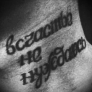 Черно-белое фото татуировки на руке с надписью на русском языке: «Счастье не нуждается». Текст выполнен каллиграфическим шрифтом.