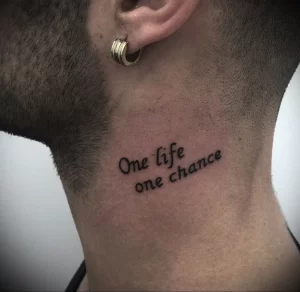 Фото тату: небольшая черная татуировка с надписью "One life one chance" на шее. Татуировка выполнена простым шрифтом, подчеркивающим ее минимализм.