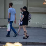 Фотография девушки с татуировками на руке и ноге, демонстрирующими рисунки паутины, кошки и цифры '199'.