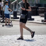 Фото девушки с татуировкой на ноге: реалистичные цветы, пчела, черно-серые тона, детальная проработка, повседневный стиль.