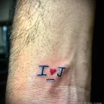 Фото миниатюрной татуировки на запястье: надпись 'I ❤️ J' с сердечком вместо буквы 'O', выполненная в ярких цветах.