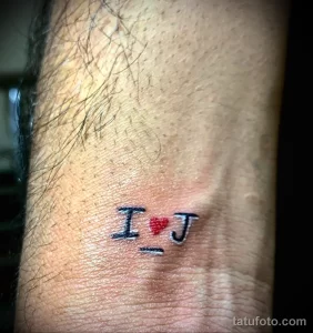 Фото миниатюрной татуировки на запястье: надпись 'I ❤️ J' с сердечком вместо буквы 'O', выполненная в ярких цветах.