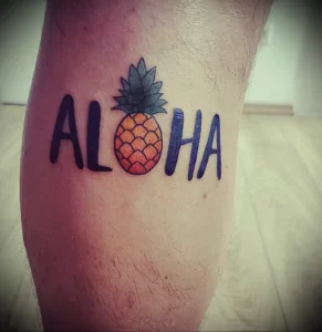 Фото тату надписи 'Aloha' с изображением ананаса. Яркие цвета и простой дизайн делают татуировку привлекательной и позитивной.