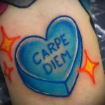Фото тату на руке с изображением голубого сердца с надписью 'Carpe Diem', украшенного оранжевыми звездами, в стиле олдскул.