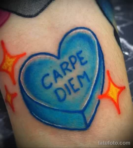 Фото тату на руке с изображением голубого сердца с надписью 'Carpe Diem', украшенного оранжевыми звездами, в стиле олдскул.