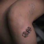 Фото тату двух игральных костей с сердечком на одной из граней. Простой и лаконичный рисунок татуировки в черно-серых тонах.