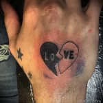 Фото тату разбитого сердца с надписью "LoVe" на руке. Минималистичный и эмоциональный рисунок в черно-белых тонах.