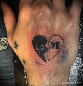 Фото тату разбитого сердца с надписью "LoVe" на руке. Минималистичный и эмоциональный рисунок в черно-белых тонах.