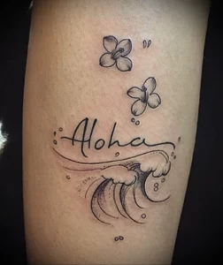 Фото тату с надписью 'Aloha', изображением волны и цветов на руке. Красивый и символичный дизайн, отражающий любовь к морю и гавайской культуре.