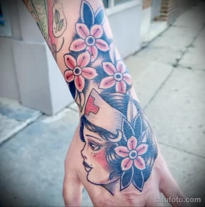 Фото тату на руке с изображением головы медсестры, окруженной розовыми цветами. Яркий и стильный рисунок татуировки.