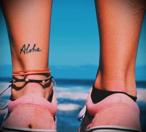 Фото тату с надписью 'Aloha' на щиколотке. Простой и элегантный дизайн, идеально подходит для тех, кто ценит минимализм.