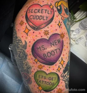 Фото тату на ноге: несколько сердец в стиле конфет 'candy heart' с забавными надписями. Цветной рисунок татуировки.