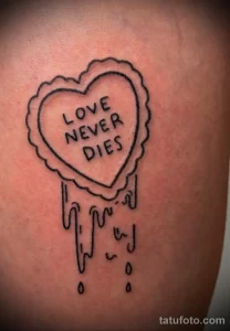 Фото тату на руке: черное сердце с надписью 'LOVE NEVER DIES'. Простой и лаконичный рисунок татуировки.