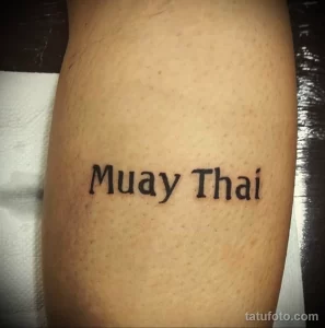 Фото тату надписи 'Muay Thai' черными чернилами на ноге. Минималистичный рисунок татуировки, выполненный опытным мастером тату.