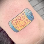 Фото яркой татуировки на руке с изображением батарейки и надписью 'Girl Power'. Использованы цвета: синий, розовый и желтый.