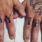Фото тату надписи 'Muay Thai' черными чернилами на пальцах рук. Детализированный рисунок татуировки, выполненный опытным мастером тату.