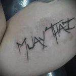 Фото тату на руке: надпись "MUAY THAI" в стиле brush lettering, выполненная в черном цвете.