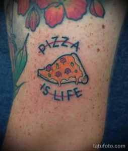 Фото татуировки с изображением куска пиццы и надписью 'Pizza is life'. Яркий рисунок татуировки в стиле традишнл.