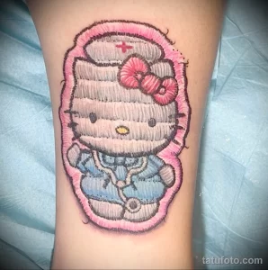 Фото милой татуировки Hello Kitty в образе медсестры с красным крестом и бантиком. Нежные розовые оттенки.