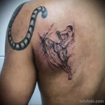 Фото тату с изображением удара ногой в стиле Muay Thai на спине. Черно-серый рисунок в эскизном стиле с добавлением брызг.