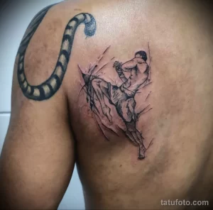 Фото тату с изображением удара ногой в стиле Muay Thai на спине. Черно-серый рисунок в эскизном стиле с добавлением брызг.