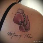 Фото тату боксерских перчаток в стиле Muay Thai на плече. Цветной рисунок с реалистичной детализацией и надписью "Muay Thai".