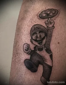 Фото тату Марио из Super Mario Bros., держащего пиццу над головой, выполненное в черно-серых тонах на руке. Ностальгический эскиз тату для поклонников видеоигр.