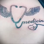 Фото тату стетоскопа с крыльями и надписью 'medicine' на фоне сердца. Минималистичный дизайн в черно-белых тонах.