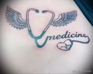 Фото тату стетоскопа с крыльями и надписью 'medicine' на фоне сердца. Минималистичный дизайн в черно-белых тонах.