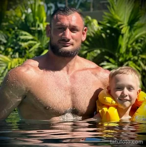 Фото мужчины с сыном в бассейне. На руке мужчины видна татуировка. Счастливый момент, демонстрирующий любовь и заботу.