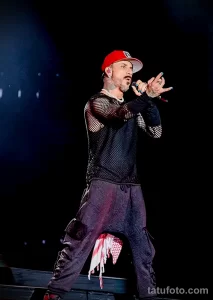 Фото солиста группы Backstreet Boys на сцене с видимыми татуировками на руках и шее.