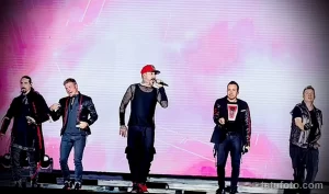 Фото группы Backstreet Boys на сцене с видимыми татуировками на руках участников.