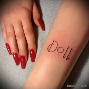 Фото тату с надписью 'Doll' на руке. Простой и лаконичный дизайн в черном цвете.