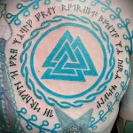 Фото тату на плече с изображением Одина, окруженного руническим кругом. Цветная татуировка с использованием ярких оттенков синего и бирюзового.